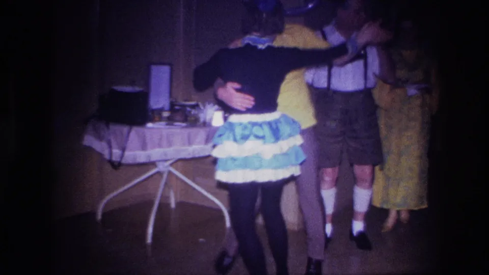 The dancing couple moves near a small refreshment table in the 1967 Ottawa interior while guests in festive clothing stand along the wall.