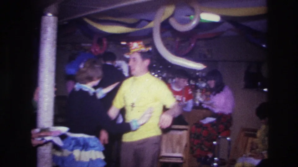1967 Ottawa party footage showing a man in a yellow shirt dancing with a woman in a blue-and-white ruffled skirt amid decorations and onlookers.