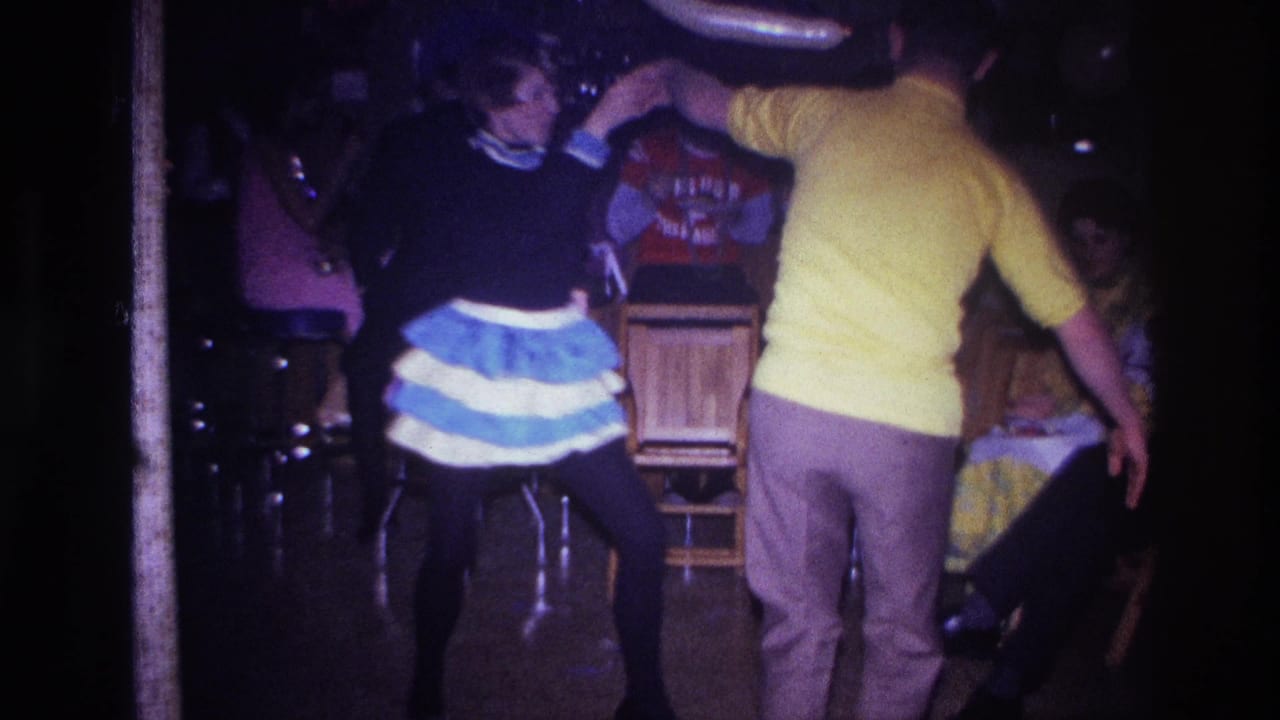In the Ottawa party scene, the couple dances near stools, tables, seated guests, and a long white balloon overhead.