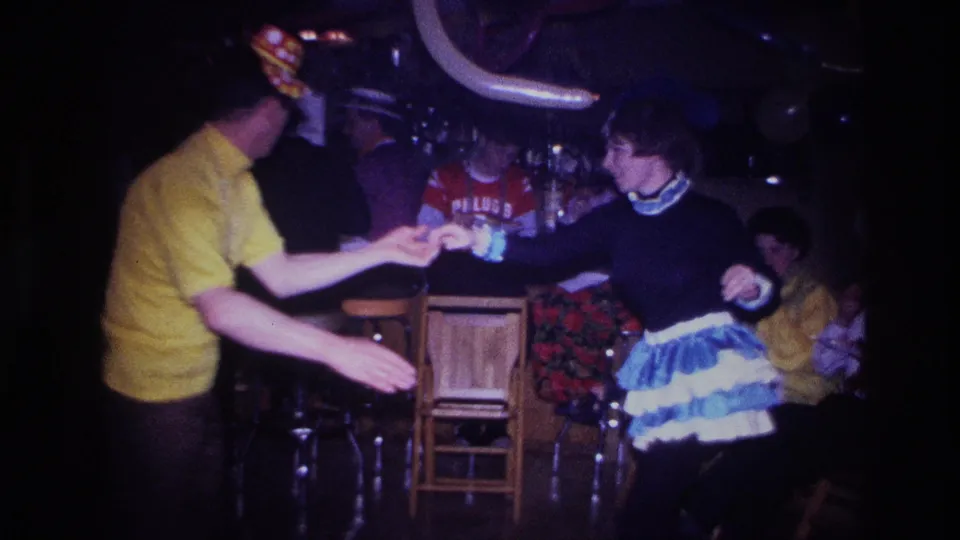 The dancers face each other in the 1967 Ottawa party interior, with seated guests and possible shirt lettering behind them.