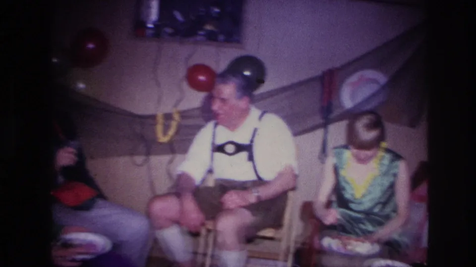 1967 Ottawa Halloween party frame with a seated man in lederhosen, a guest in green costume, balloons, and home wall decorations.