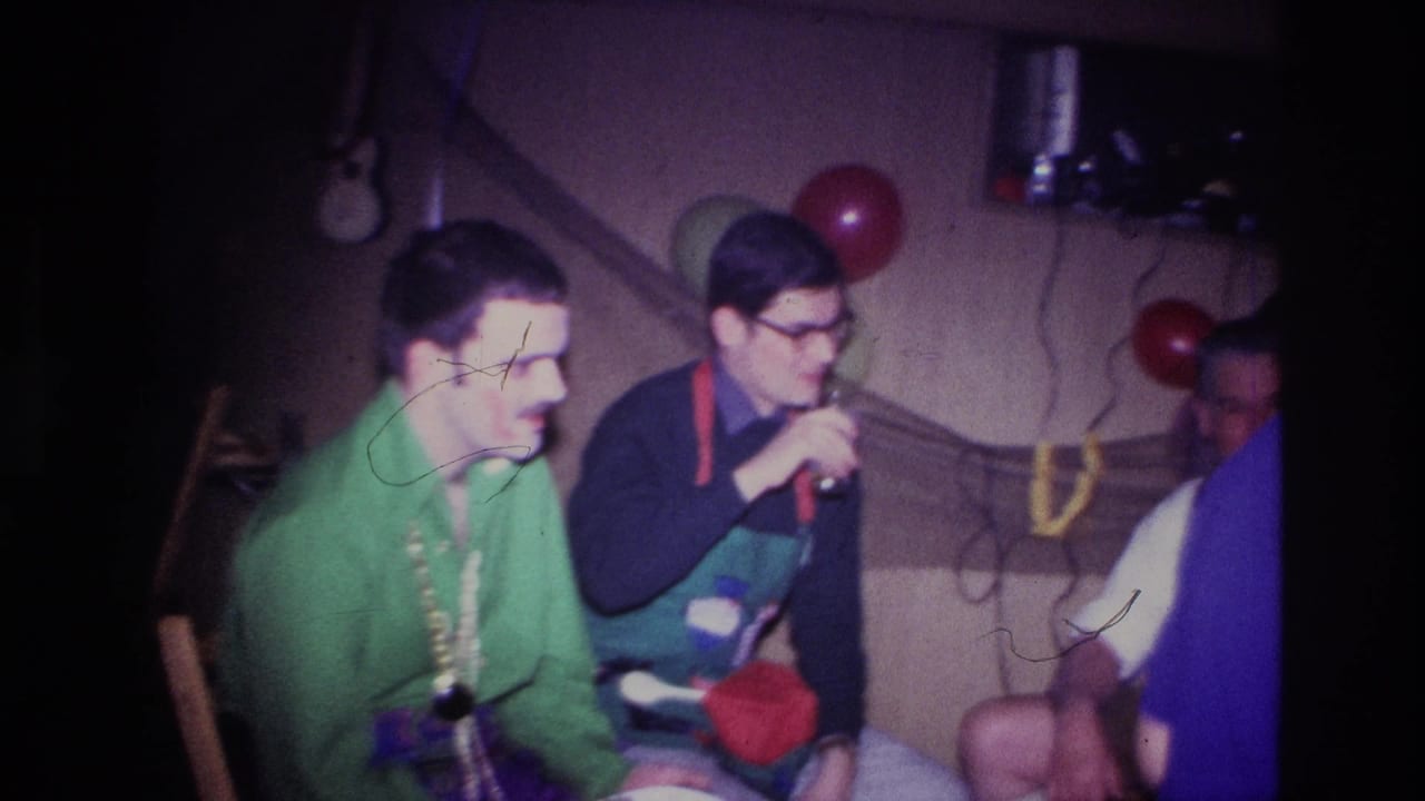 1967 Ottawa party frame with a man in a green shirt and beads beside another seated man, with balloons and a private interior wall behind them.