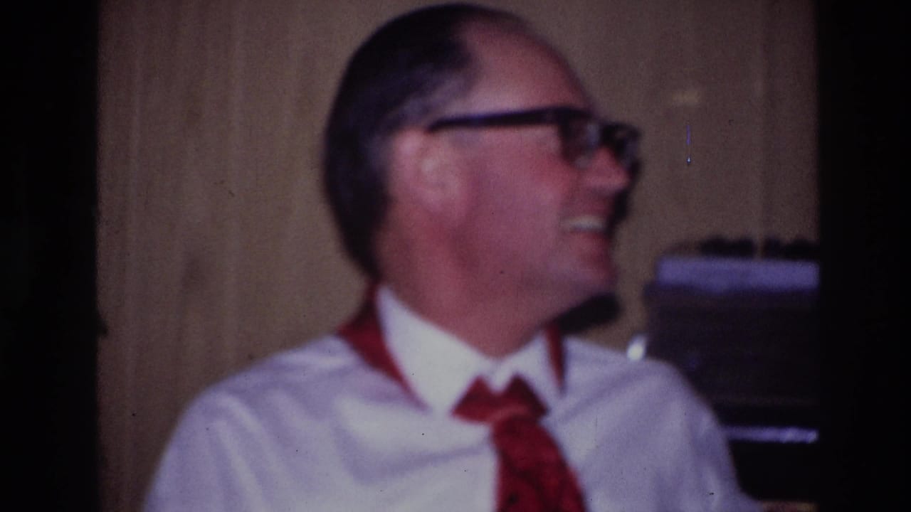 Ottawa 1967 frame showing a seated man in thick-rimmed glasses laughing in a warm, wood-paneled private interior.