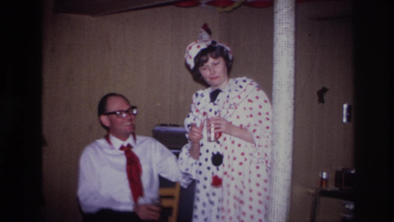 In 1967 Ottawa home-movie footage, a woman in a white polka-dot clown costume stands near a seated man during an indoor party.
