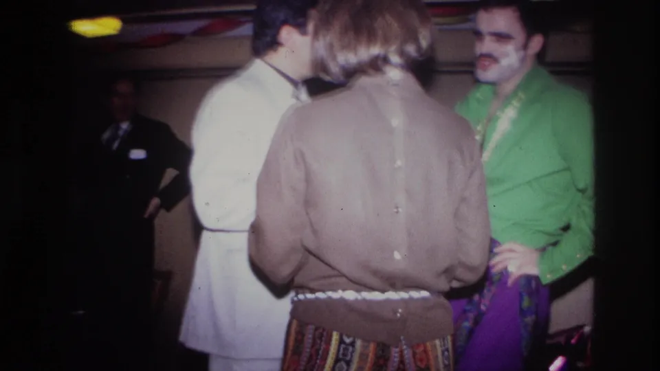 In Ottawa, Canada in 1967, adults gather at a dim private party, including a man in a green shirt, a person in a brown sweater, and a white suit.