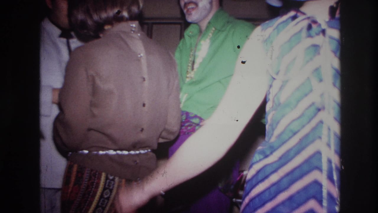 Party guests stand close together, including a green shirt and a striped dress in the foreground.