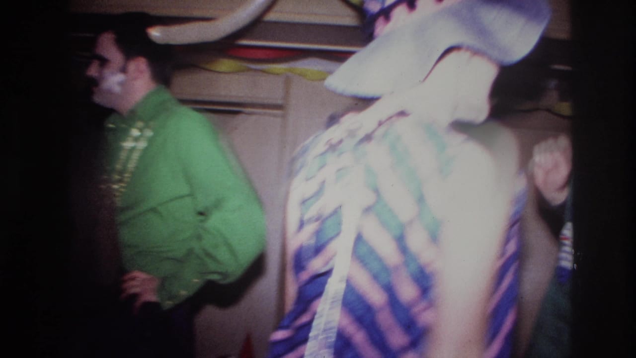 Guests in a dim party room, including a man in green and a bright costumed figure in the foreground.