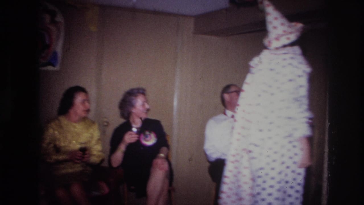 Seated adults watch a clown in a polka-dot costume at an indoor party.