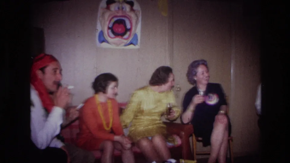 Adults seated in an Ottawa party interior smile and look toward the performer, with a clown-face decoration hanging on the wall behind them.