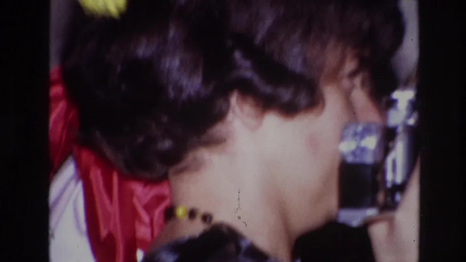 A soft 8mm close-up shows the woman and camera from the side, with red decoration and another guest behind her.
