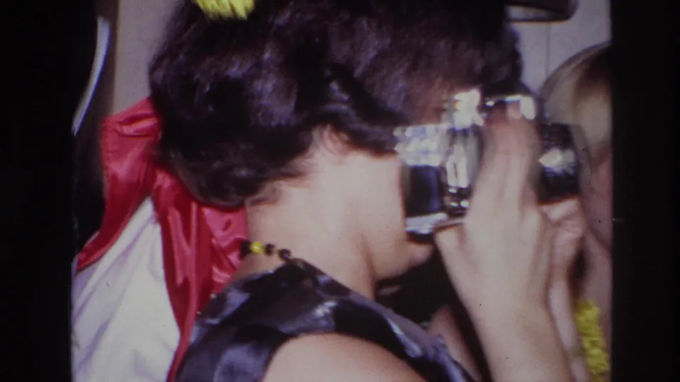 In the final frame, the woman keeps the camera at eye level amid yellow garland, red fabric, and nearby party guests.