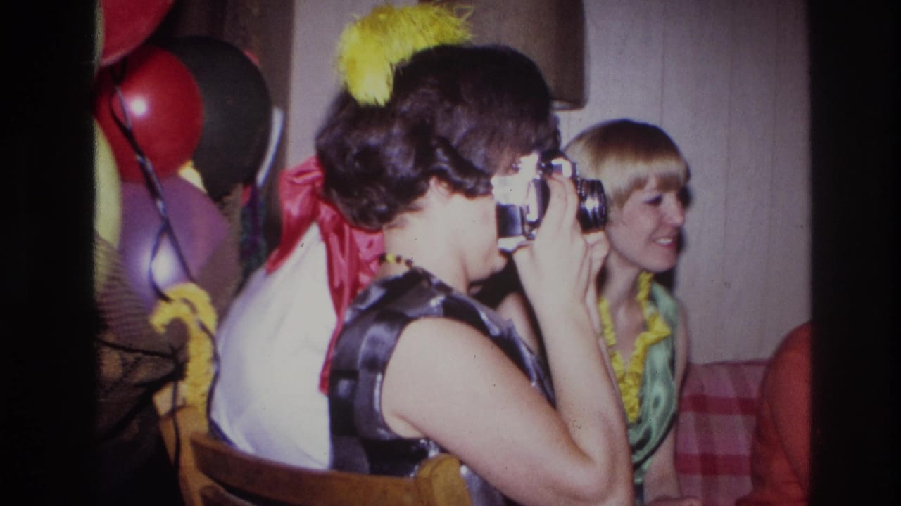 The woman continues aiming her camera during the Ottawa party, with a smiling blonde guest, balloons, and indoor decorations visible behind her.