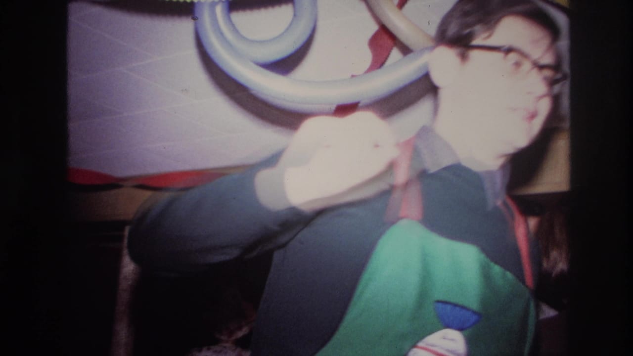 1967 Ottawa home-movie frame of a man in glasses near balloons and streamers at an indoor party.