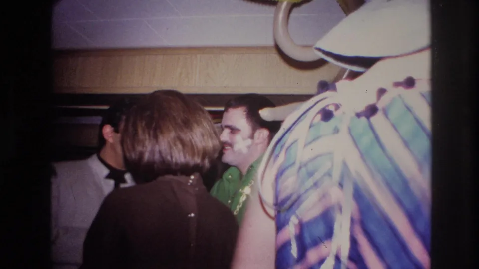 1967 Ottawa indoor party frame showing adults talking, with balloons overhead and shaving cream on one guest's face.