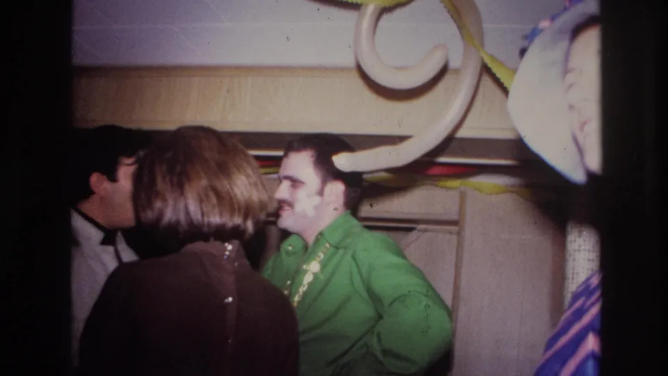 1967 Ottawa home-movie frame of adults at a house party, with balloons and a smiling man in green partly covered in shaving cream.