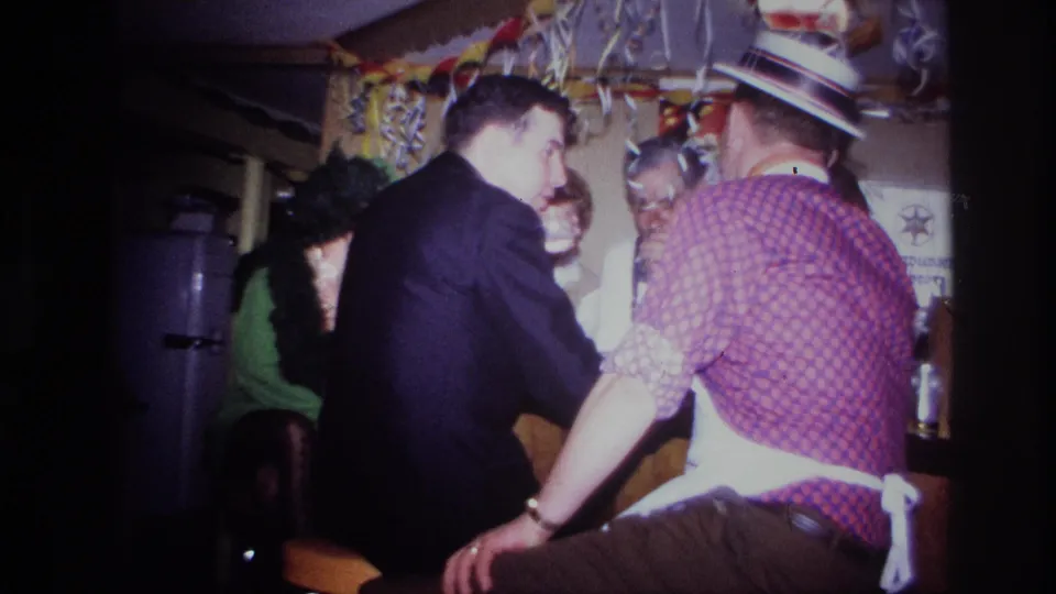 1967 Ottawa party frame with a suited man leaning into a bar area and a seated man in a checkered shirt and straw hat.