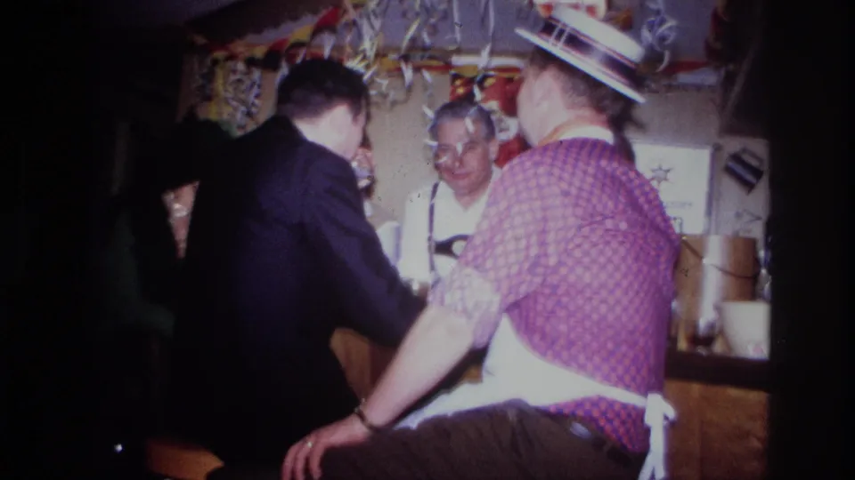 1967 Ottawa indoor party frame showing adults around a wooden bar, including a man in suspenders and a man in a straw hat.