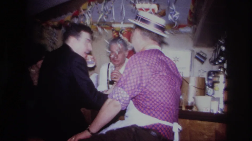 Home-movie view of a 1967 Ottawa bar gathering, with a suited man leaning forward and aproned men behind the counter.