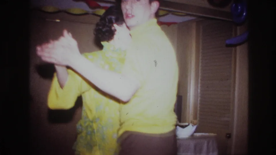 Close 1967 Ottawa party frame of two adults dancing in a home interior, with bright yellow clothing and soft 8mm exposure.