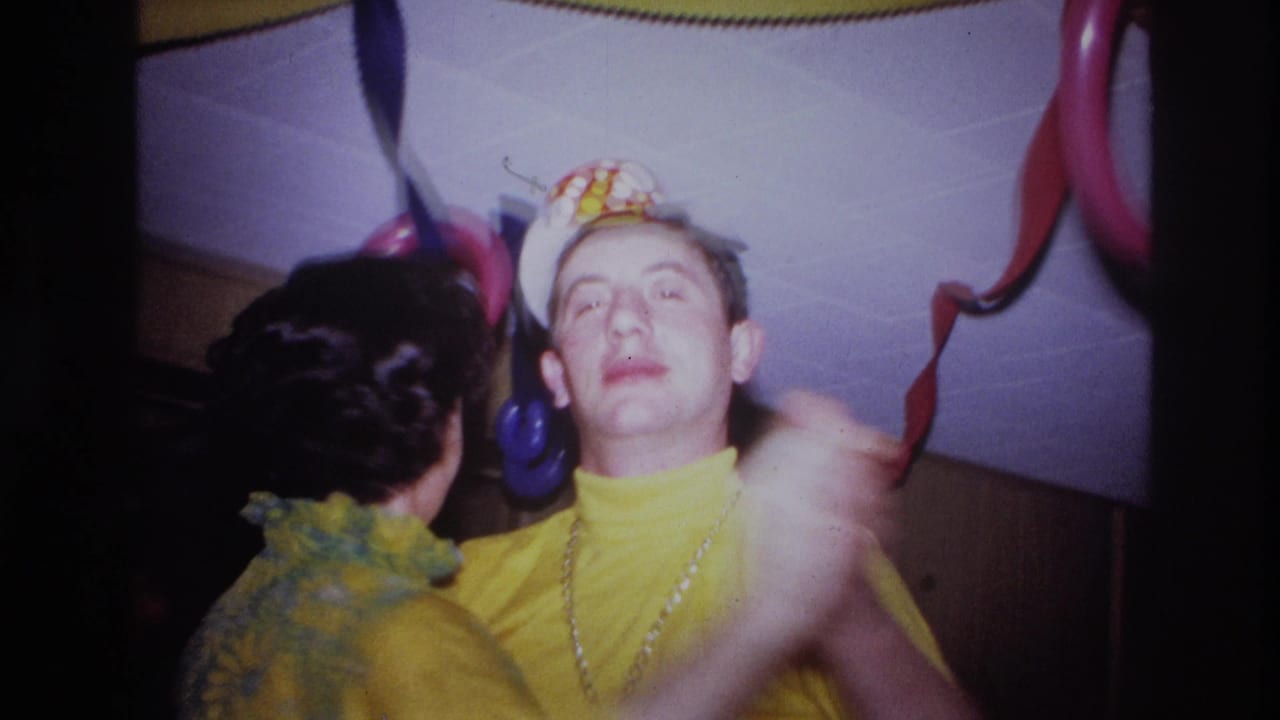 In this 1967 Ottawa home-movie frame, two adults in yellow party outfits dance closely beneath streamers and balloon decorations.