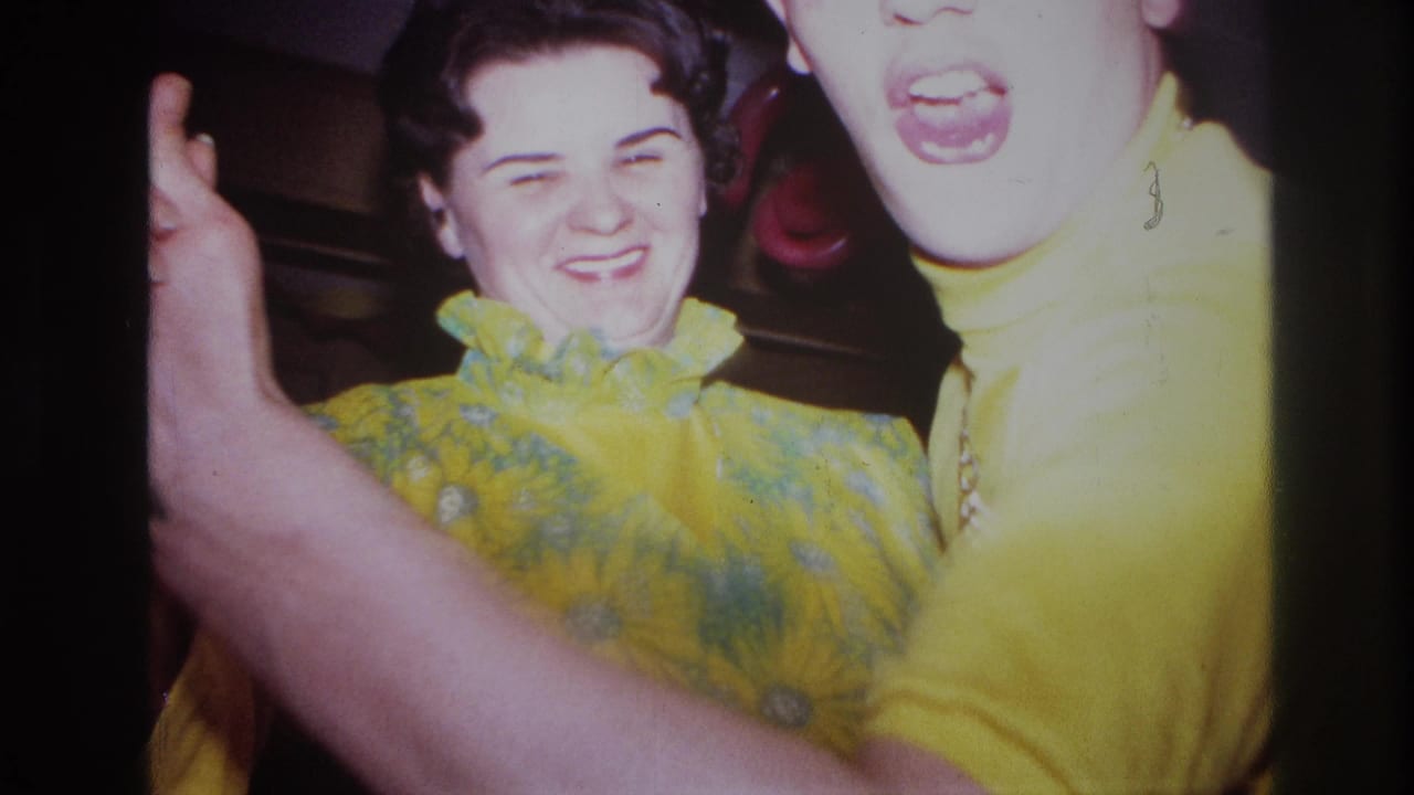 In 1967 Ottawa home-movie footage, two adults in bright yellow outfits laugh and dance near the camera inside a decorated room.