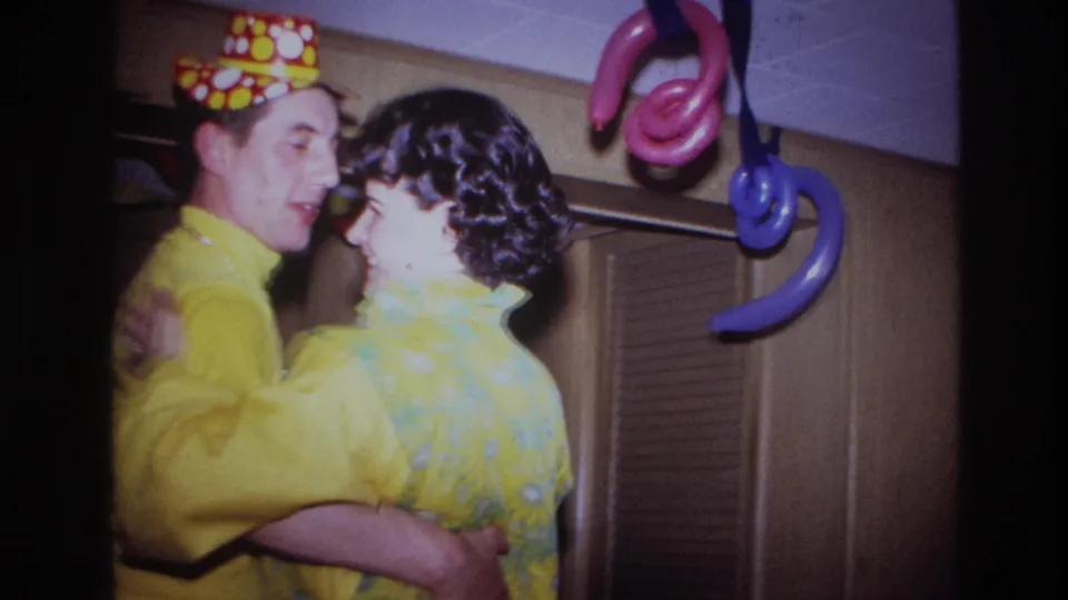 In the 1967 Ottawa home movie, the couple dances beneath colorful twisted balloon decorations beside wood paneling and closet doors.