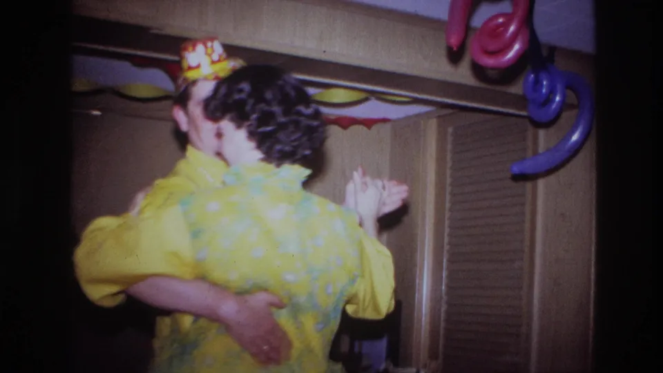 In a 1967 Ottawa home-movie frame, a young man and his mother dance under paper streamers and balloons in a decorated room.