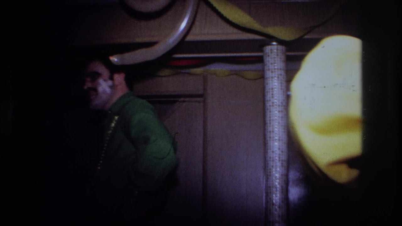 Man in a green shirt smiles near a doorway in a dim party room with streamers.