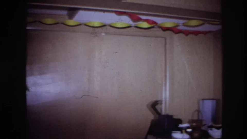 1967 Ottawa home-movie frame of a wood-paneled private party room with red and yellow streamers and small furnishings along the lower edge.