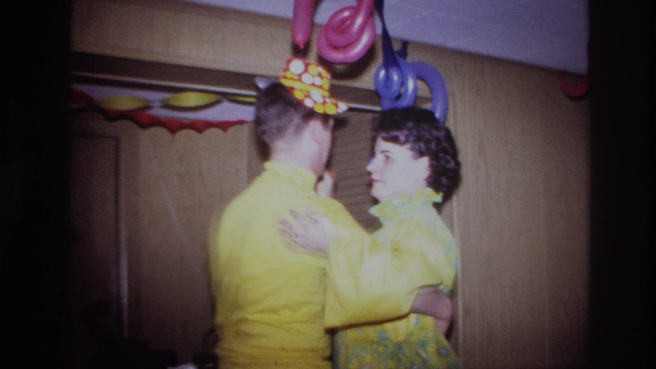 Two adults in yellow attire dance beneath colorful party decorations indoors.
