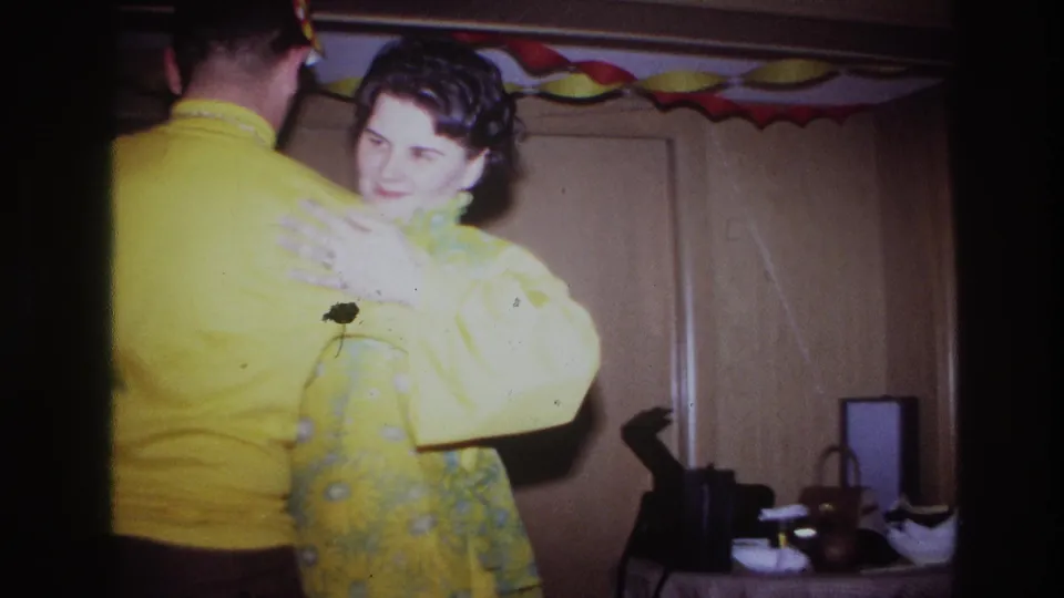 Ottawa 1967 party frame with the couple in yellow dancing close to the camera, framed by wood doors, decorations, and small household objects.