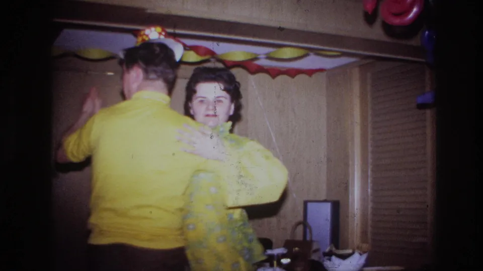 A woman in a yellow floral dress faces the camera while dancing with a man in yellow at the Ottawa home party.