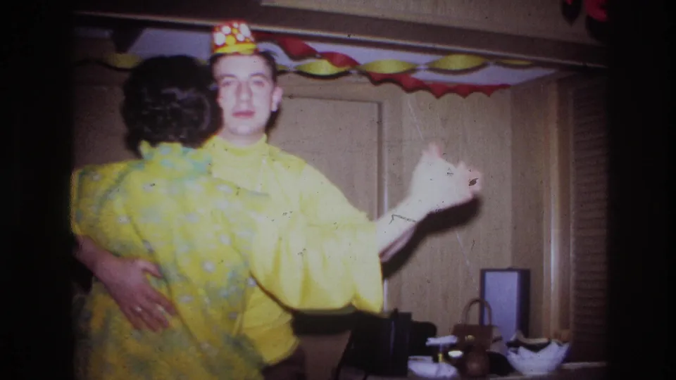1967 Ottawa home-movie frame of a couple dancing at an indoor celebration, surrounded by colorful paper decorations and wood-paneled walls.