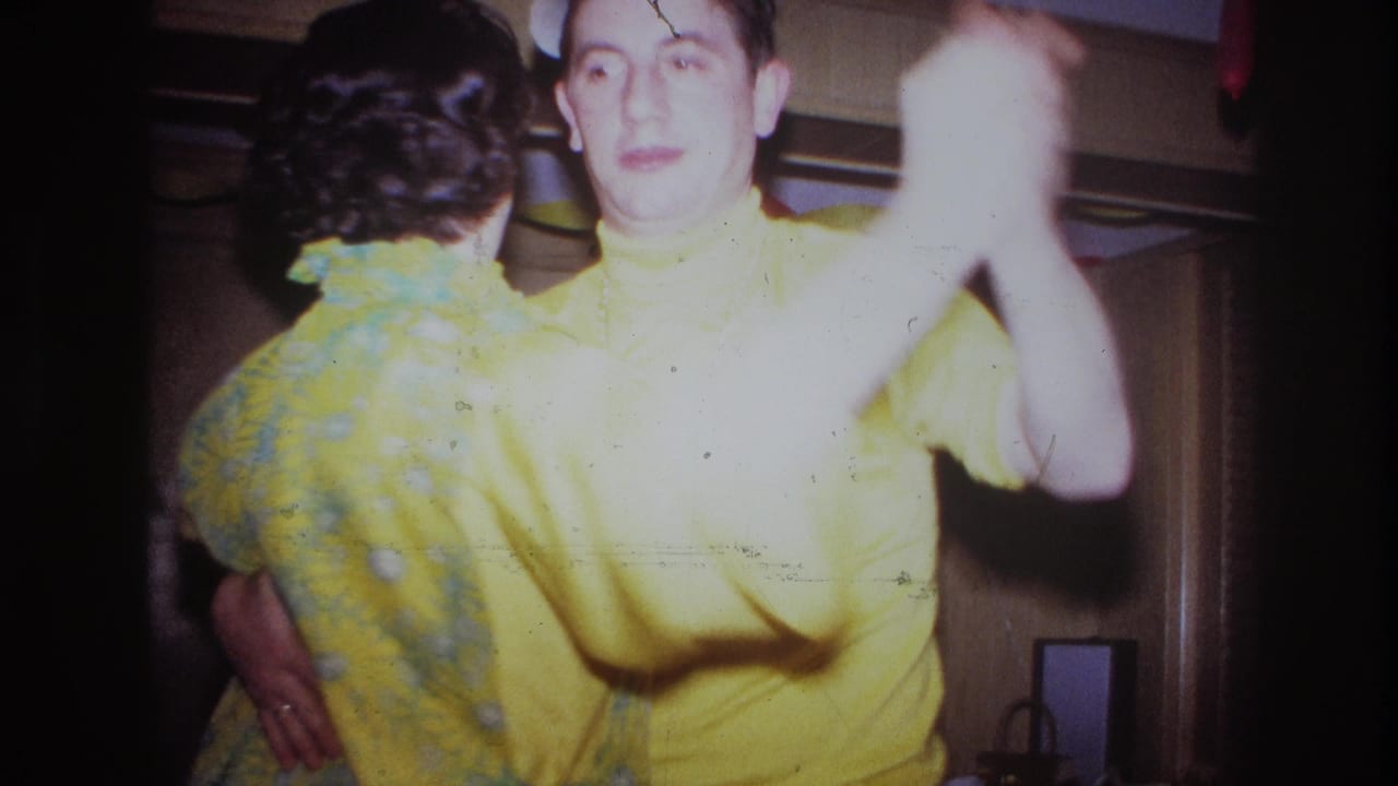 Man in a yellow shirt dances with a woman as his raised arm moves close to the lens.