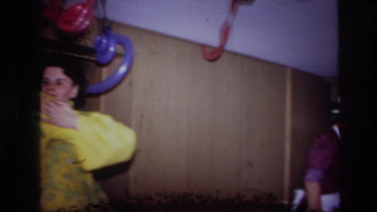 1967 Ottawa 8mm frame showing a woman in yellow at the left of a dim interior with colored hanging fixtures and visible film damage.