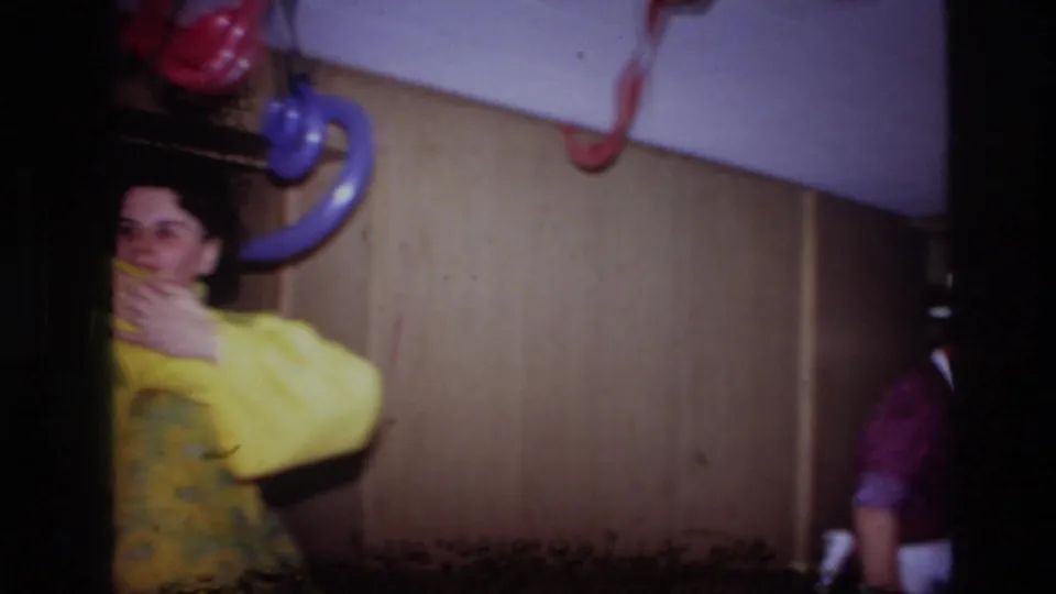 1967 Ottawa 8mm frame showing a woman in yellow at the left of a dim interior with colored hanging fixtures and visible film damage.