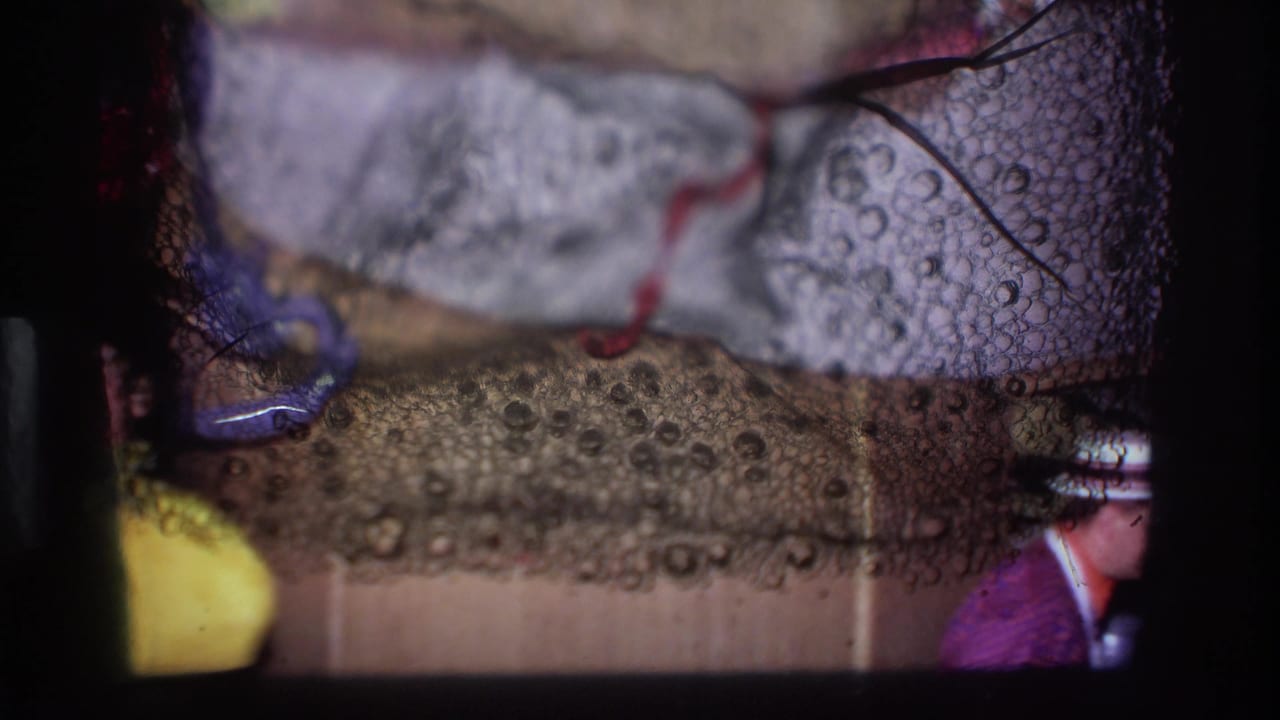 1967 Ottawa 8mm frame with heavy film debris, dark borders, and a partially visible person near a pale surface and red cord.