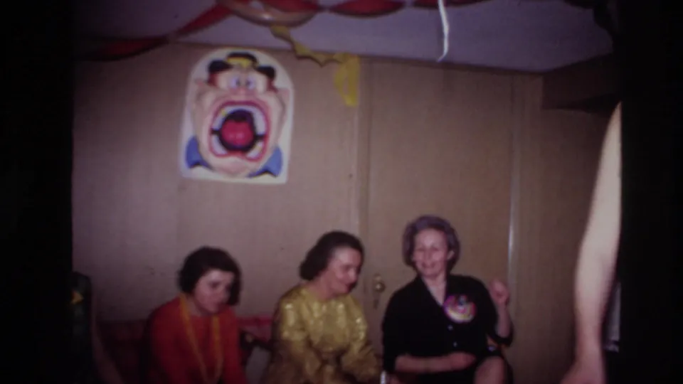 Three adult women sit on a couch in a 1967 Ottawa party interior, with a clown poster and streamers above them.
