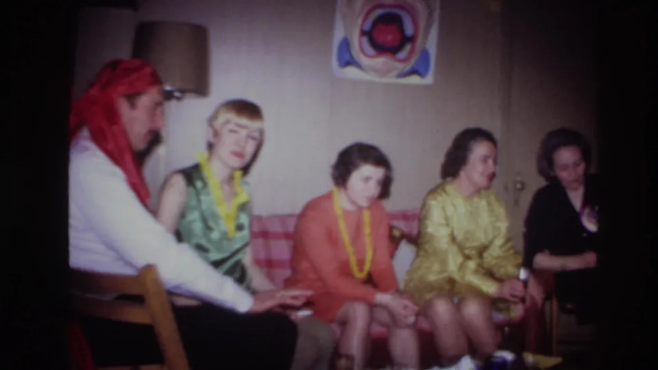 A man in a red bandana joins women seated on a couch in the 1967 Ottawa birthday party interior.