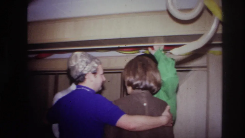 At the 1967 Ottawa party, two guests face away from the camera with an arm around one another below balloons and paper streamers.