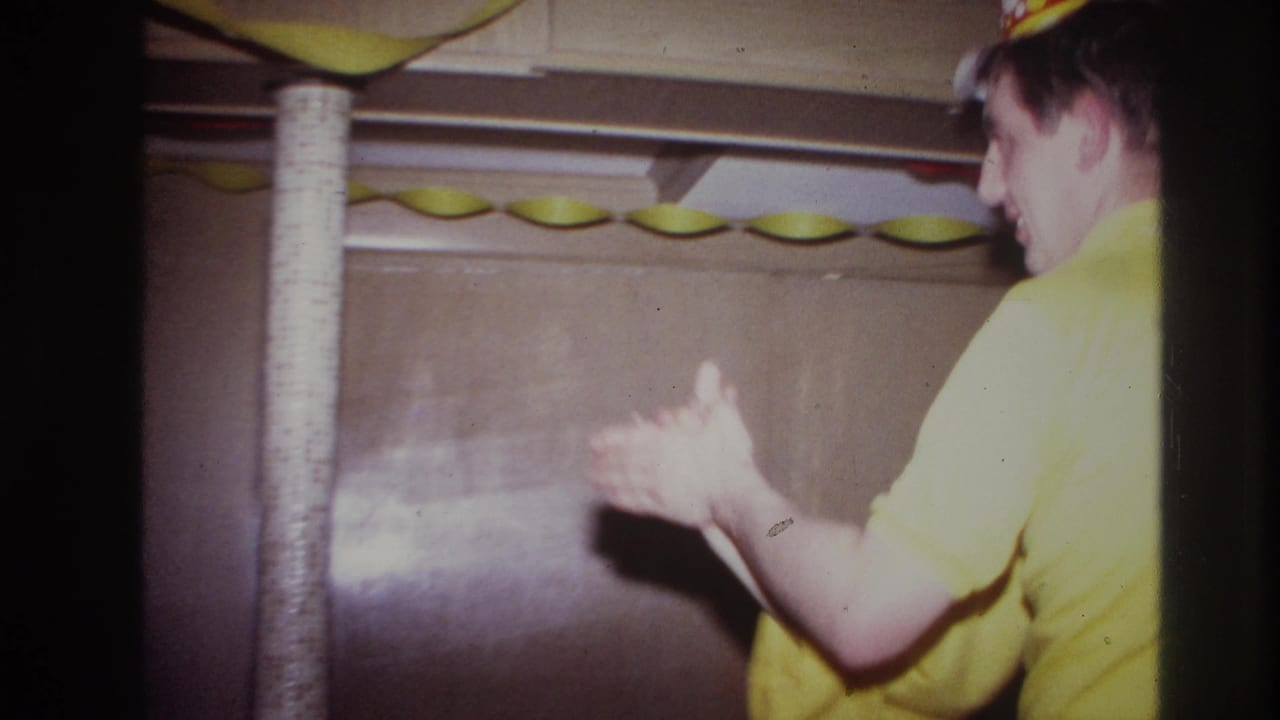 In a 1967 Ottawa home movie frame, a young couple dance closely in a small decorated room with paper streamers overhead.