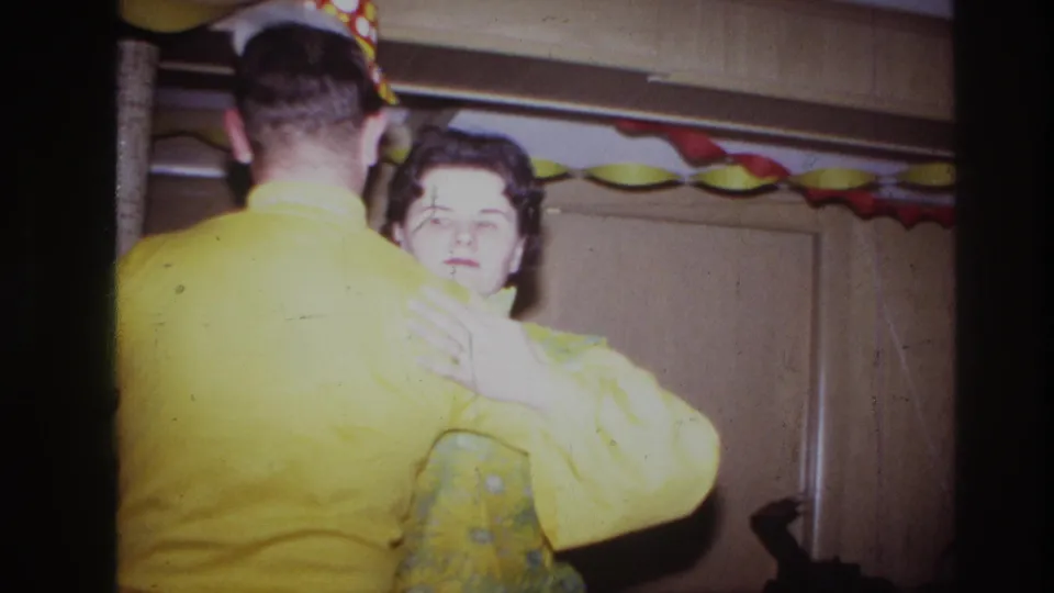 The woman looks toward the camera while dancing with the man in a yellow shirt, framed by party streamers and 8mm edge darkness.