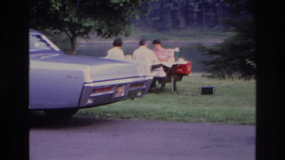1967 Ottawa lakeside picnic frame with the sedan rear in the foreground and three people seated at a table near a red cooler.