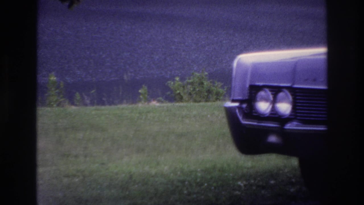 1967 Ottawa frame with a classic sedan nose entering from the right, seen through a dark window frame over a grassy area.