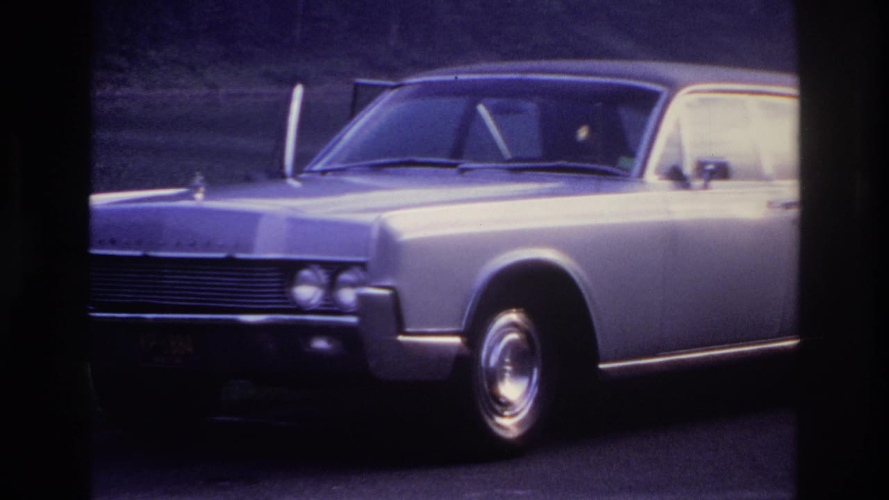 Silver sedan parked beside a road with wooded slope in the background.