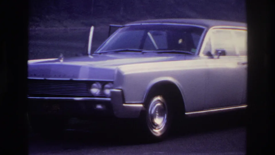 Silver sedan parked near water and trees in Ottawa, 1967, seen in soft 8mm color with bright exposure on the rear side.