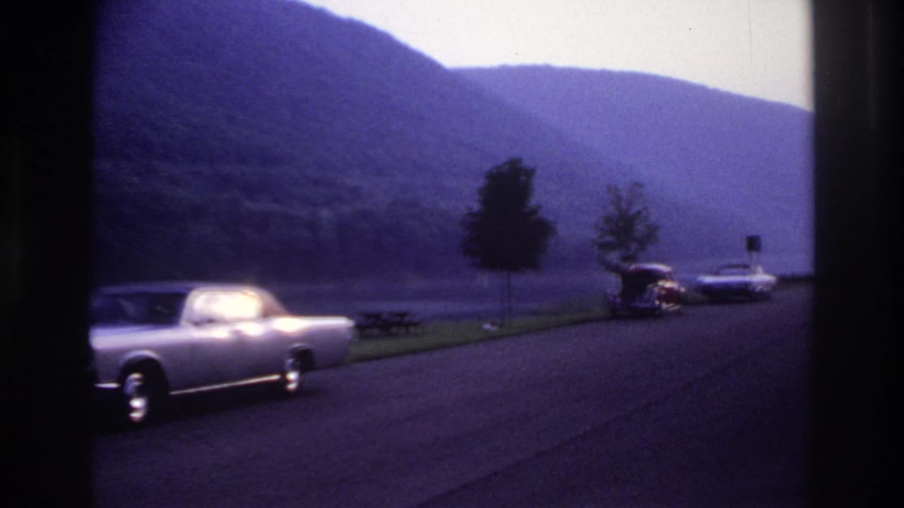 A silver mid-century car drives past a lakeside picnic area in supplied 1967 Ottawa home-movie footage.