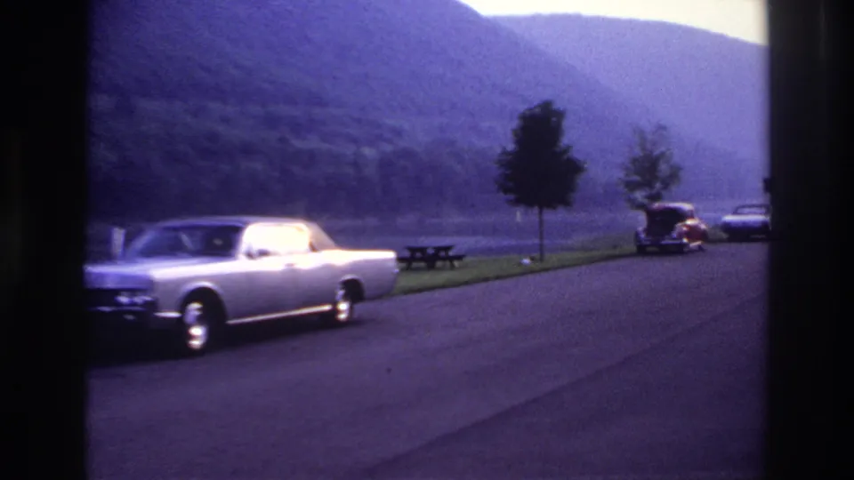 A silver convertible passes a lakeside recreation area with parked cars and picnic tables, consistent with the 1967 Ottawa metadata.