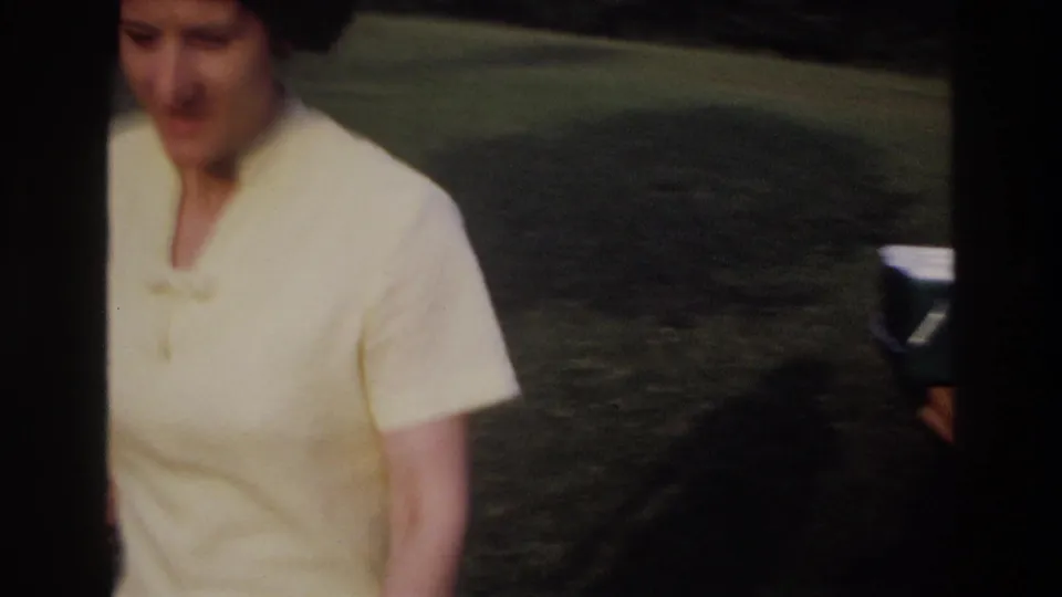 A woman in a light blouse stands close to the camera in the grassy picnic area, with the background softly out of focus.