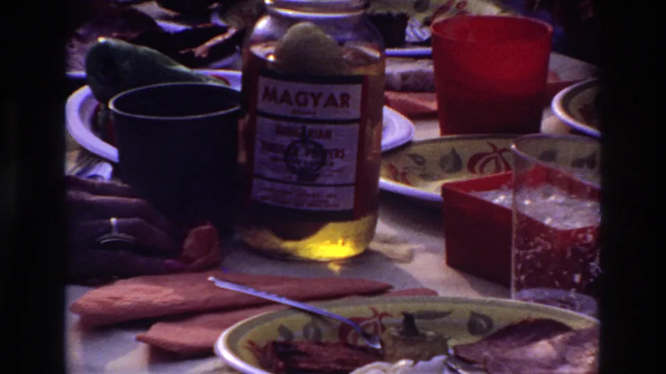 Darker 8mm close-up of the Ottawa family picnic table with a Magyar jar, red cup, blue cup, napkins, and plates of food.